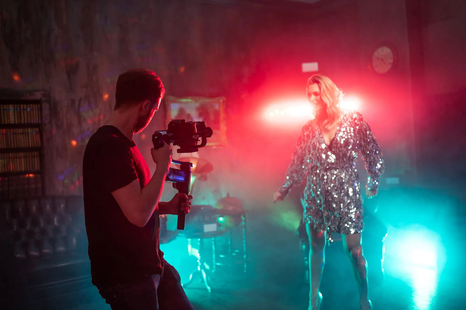 Music video shoot: a camera operator with a gimbal filming a performer in a sequin dress under red and teal light